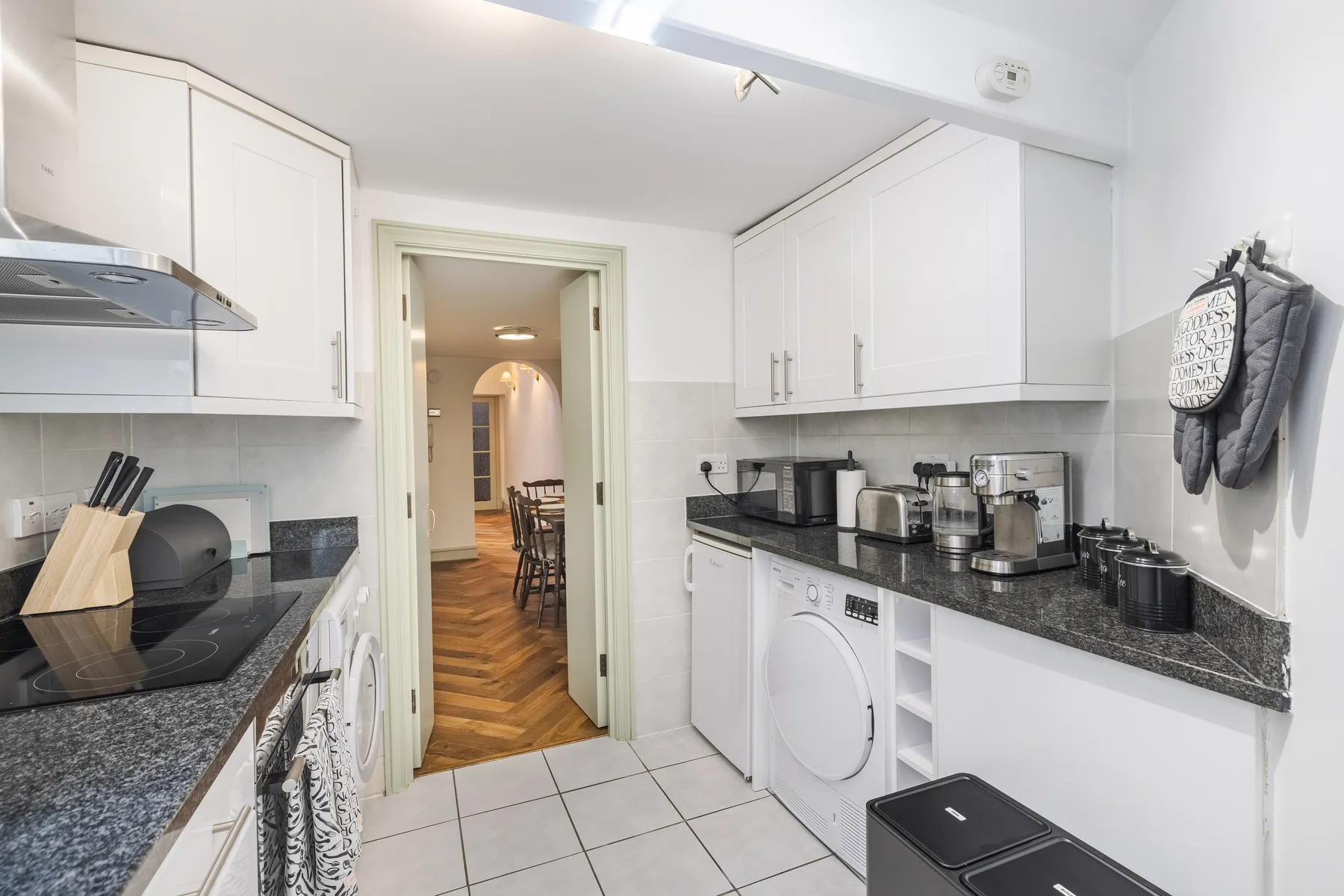 A bright kitchen with white cabinets, dark countertops, and a tiled floor.