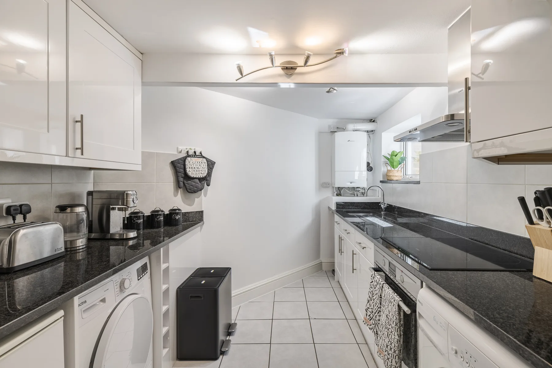 A bright kitchen with dark countertops, white cabinets, and a tiled floor.