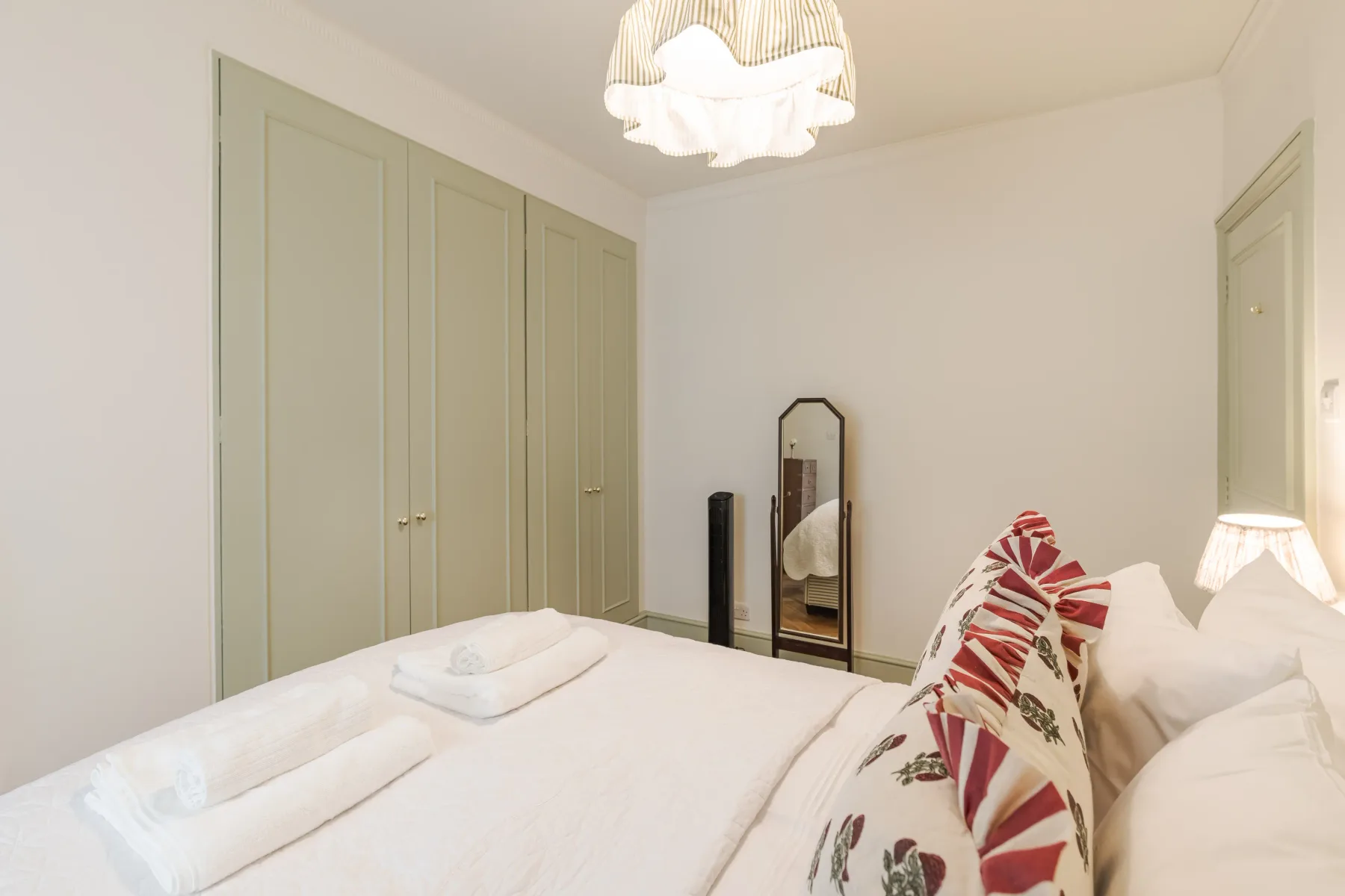 A bright bedroom with a neatly made bed and pale built-in wardrobes.