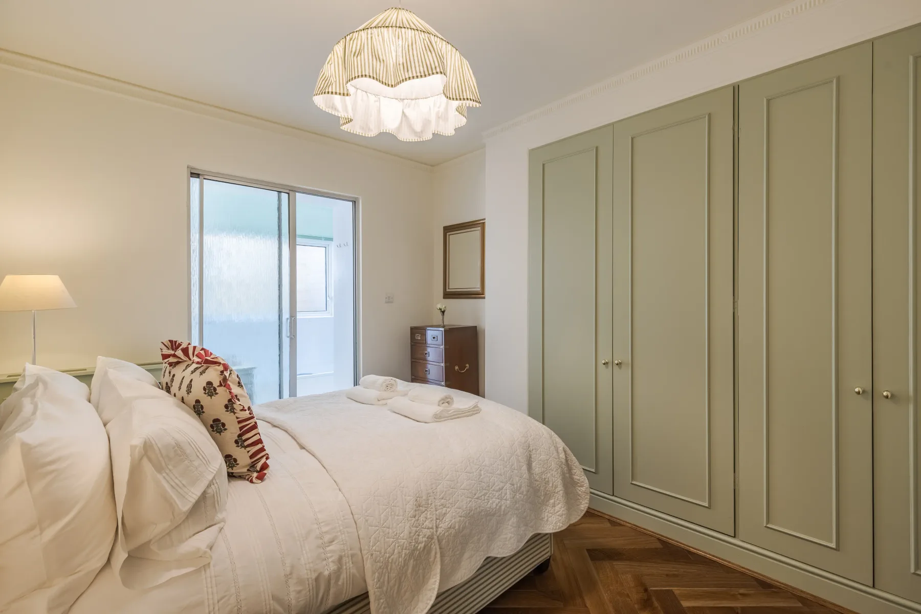 A bedroom with a bed, built-in wardrobes, and a sliding glass door.