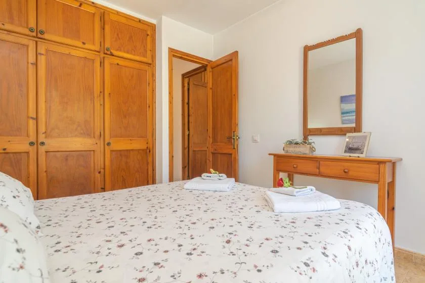 A bedroom with a patterned bedspread, wooden wardrobes, and a dressing table.