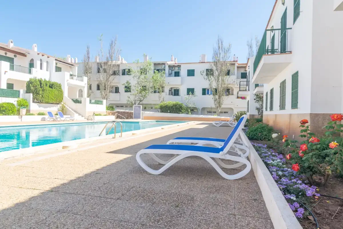 An outdoor swimming pool beside white buildings and a blue lounge chair.