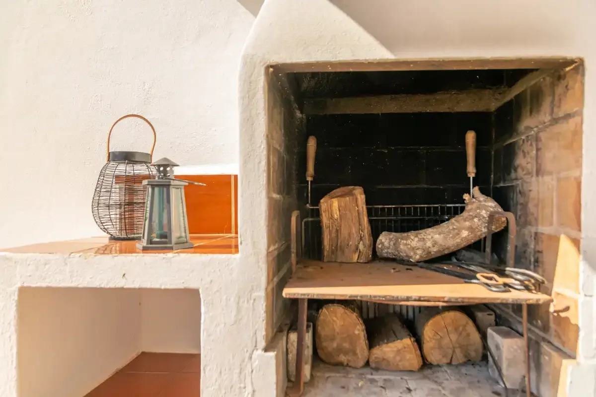 A built-in fireplace contains stacked firewood and tools.