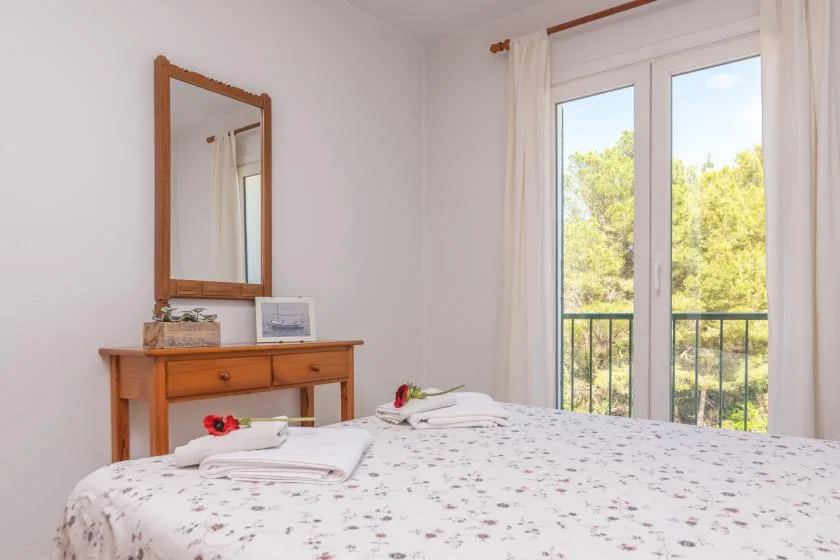 A bright bedroom has a patterned bed beside a window opening onto greenery.