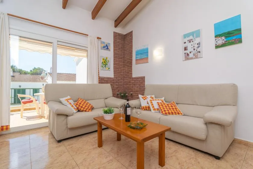 A bright living room with seating, a wooden coffee table, and glass doors opening to a balcony.