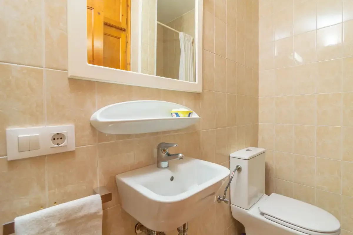 A tiled bathroom with a sink, mirror, and toilet.