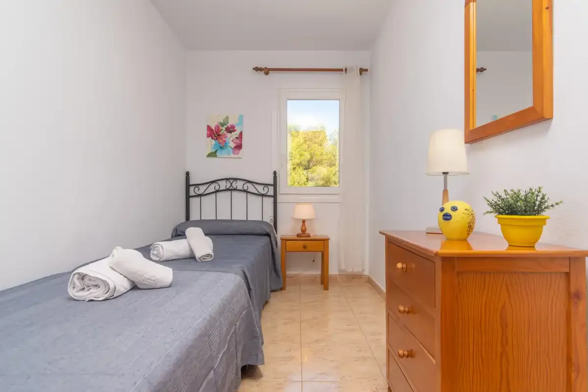 A bedroom with a bed and a wooden dresser beside the window.