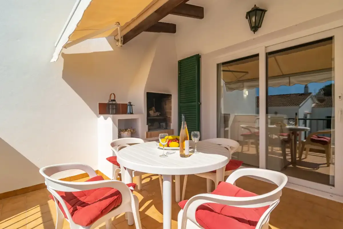 A sunny terrace with a round dining table and cushioned seating.