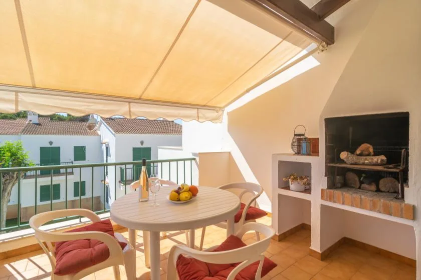 A shaded outdoor dining area with a round table and built-in barbecue.