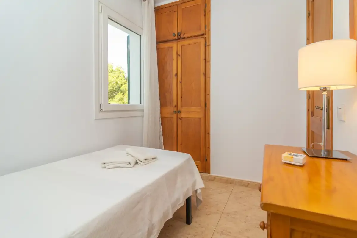 A bedroom with a neatly made bed, wooden wardrobe, and bedside lamp.