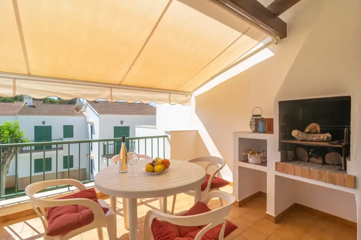 A covered outdoor dining area with a round table, seating, and a built-in grill.