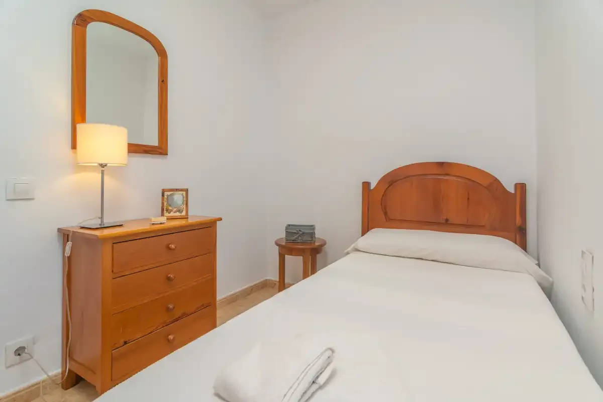 A bedroom with a wooden bed, dresser, and bedside table.