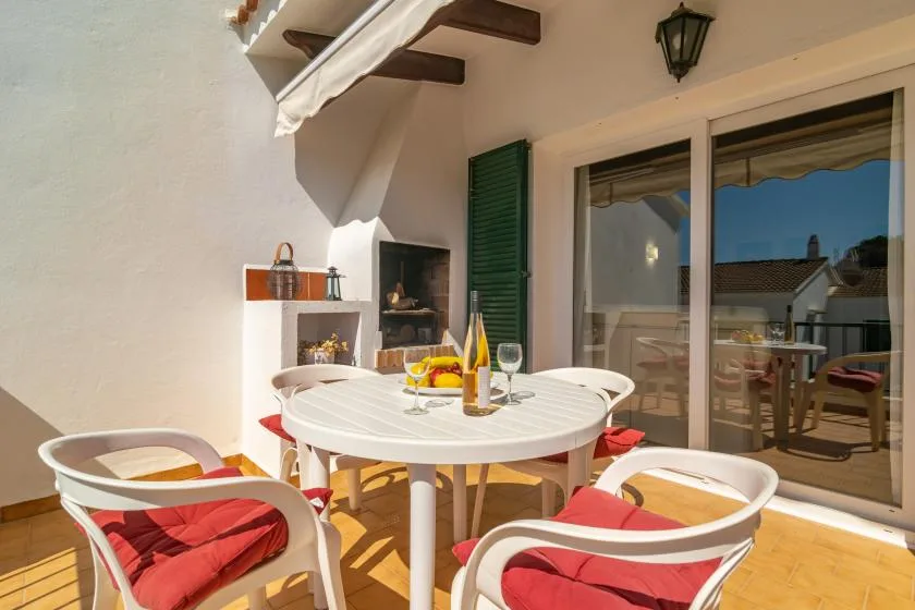 A sunny patio with a round table and red-cushioned seating beside sliding glass doors.