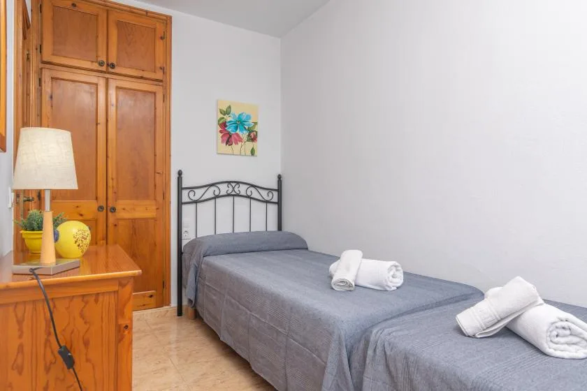 A bedroom with a single bed, wooden wardrobes, and a small colorful wall picture.