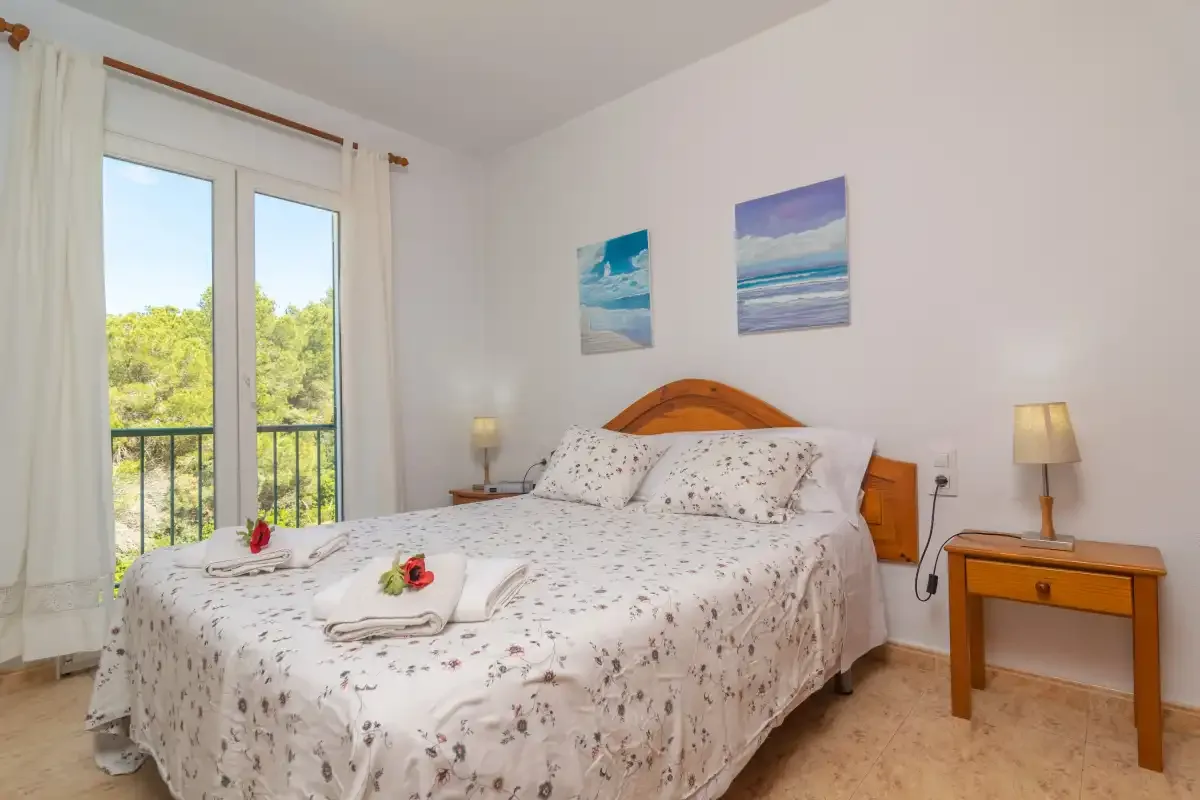A bedroom with a double bed and a large window overlooking greenery.