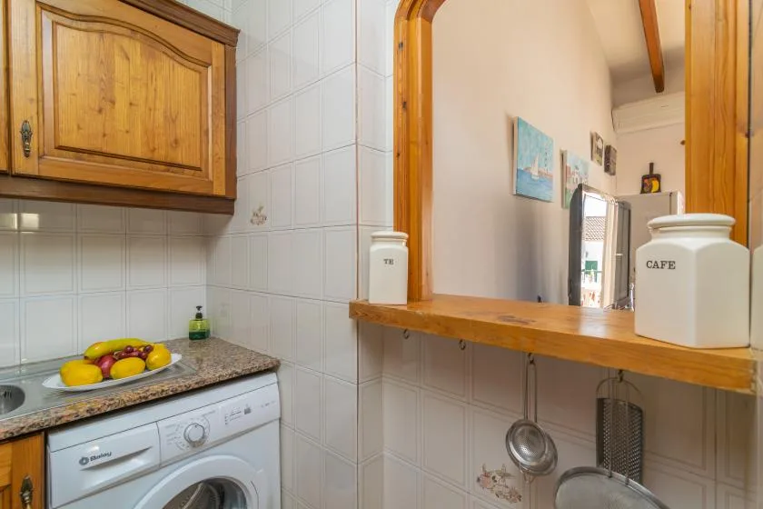 A compact kitchen with a washing machine, countertop, and wooden pass-through shelf.
