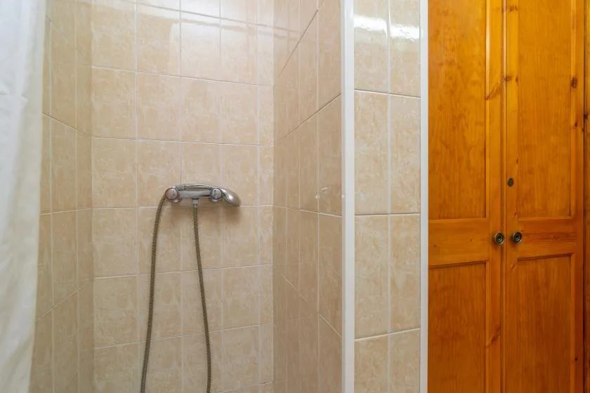 A tiled shower area with a wall-mounted shower fixture beside a wooden cabinet.