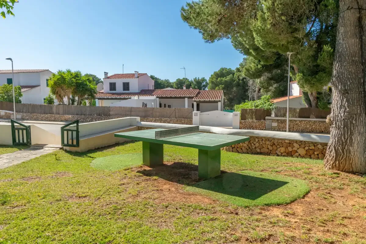 An outdoor recreation area with a green ping-pong table and a low stone wall.