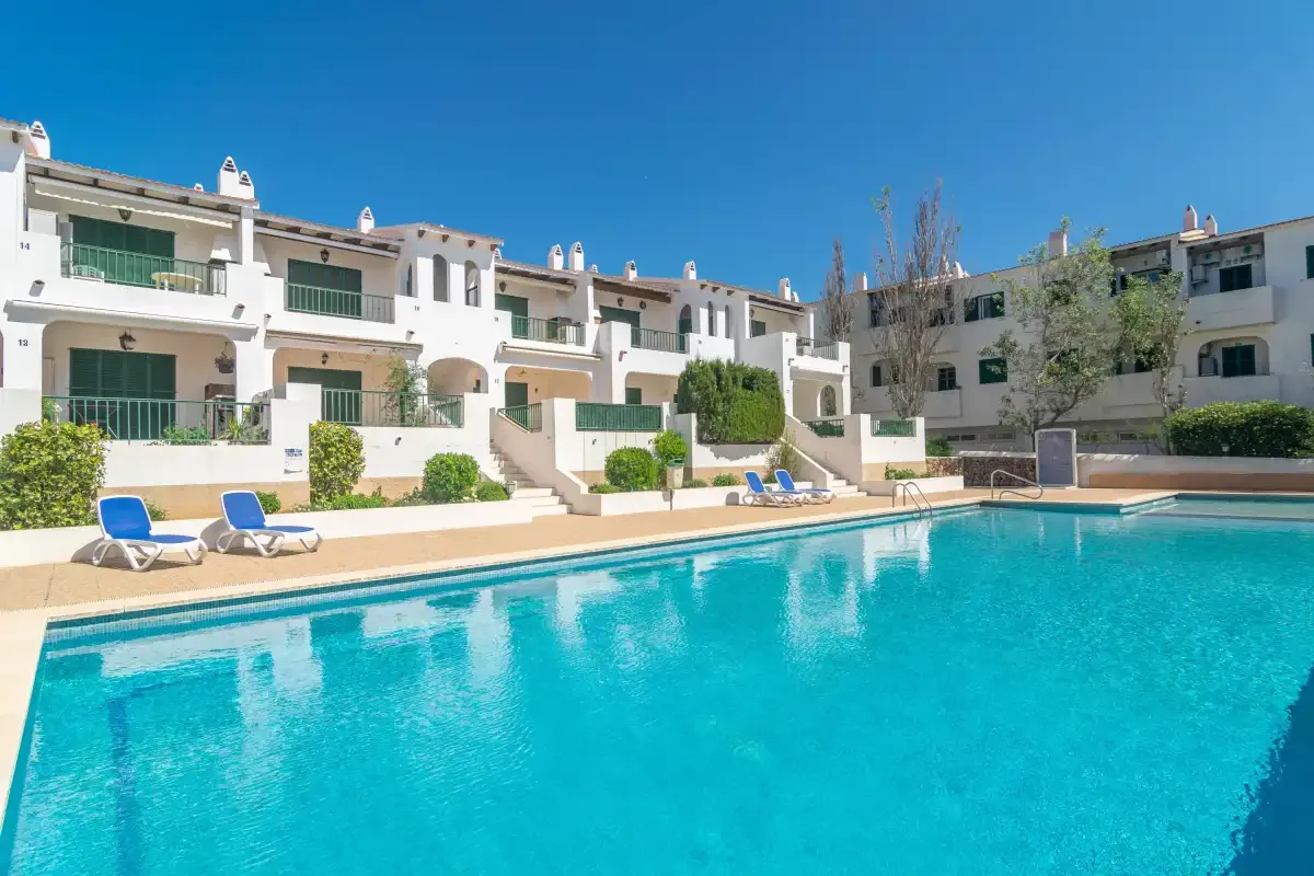 A swimming pool in front of white residential buildings under a clear blue sky.