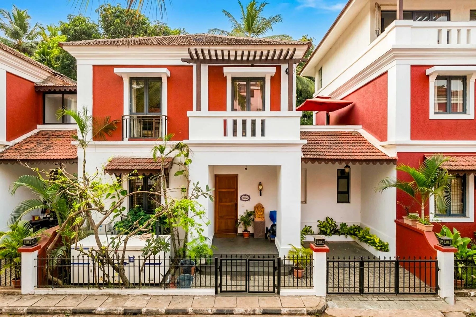 Una casa de dos plantas roja y blanca se alza tras una verja metálica negra.