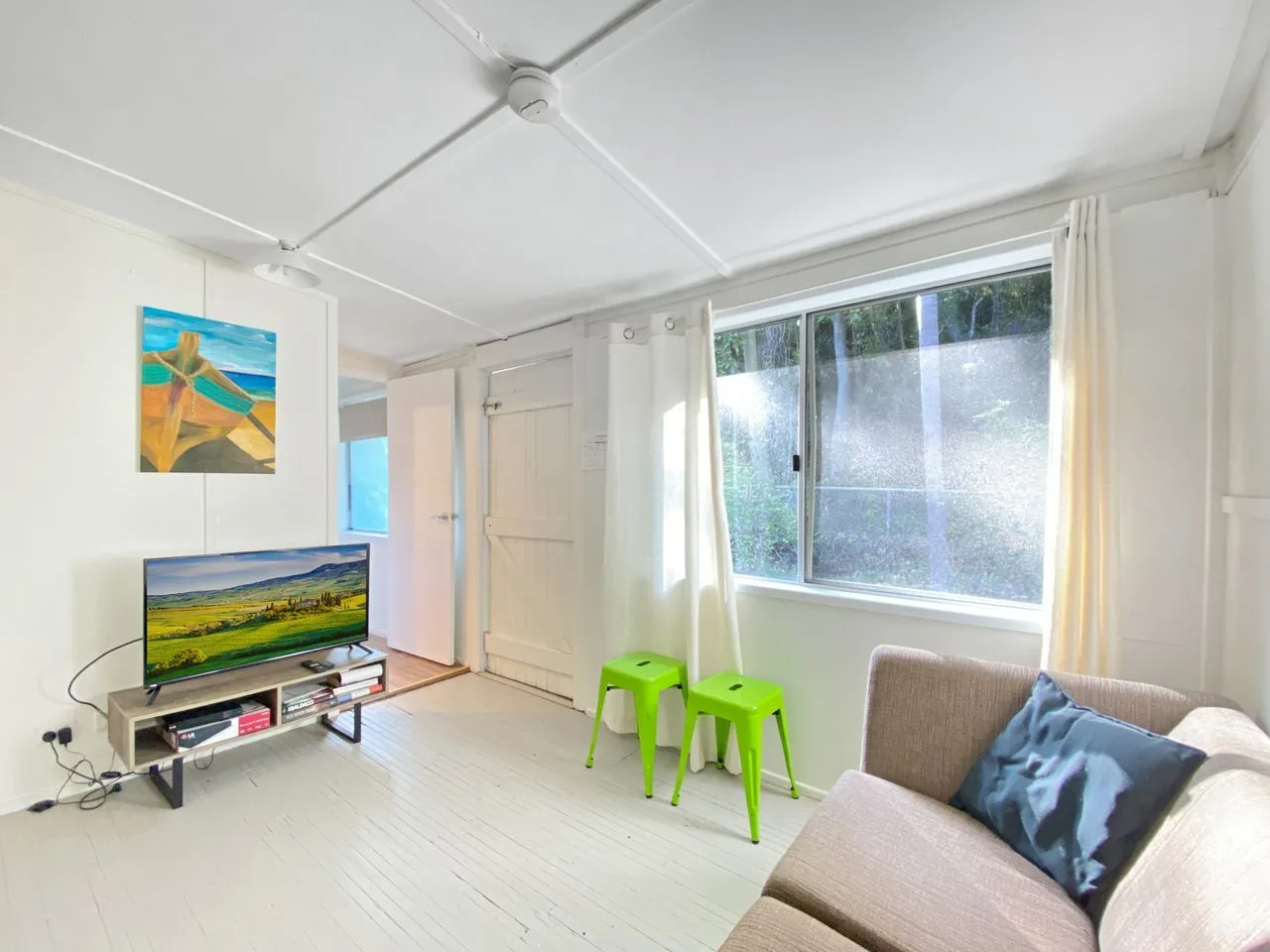 Una sala luminosa con asientos, un televisor y una ventana grande.
