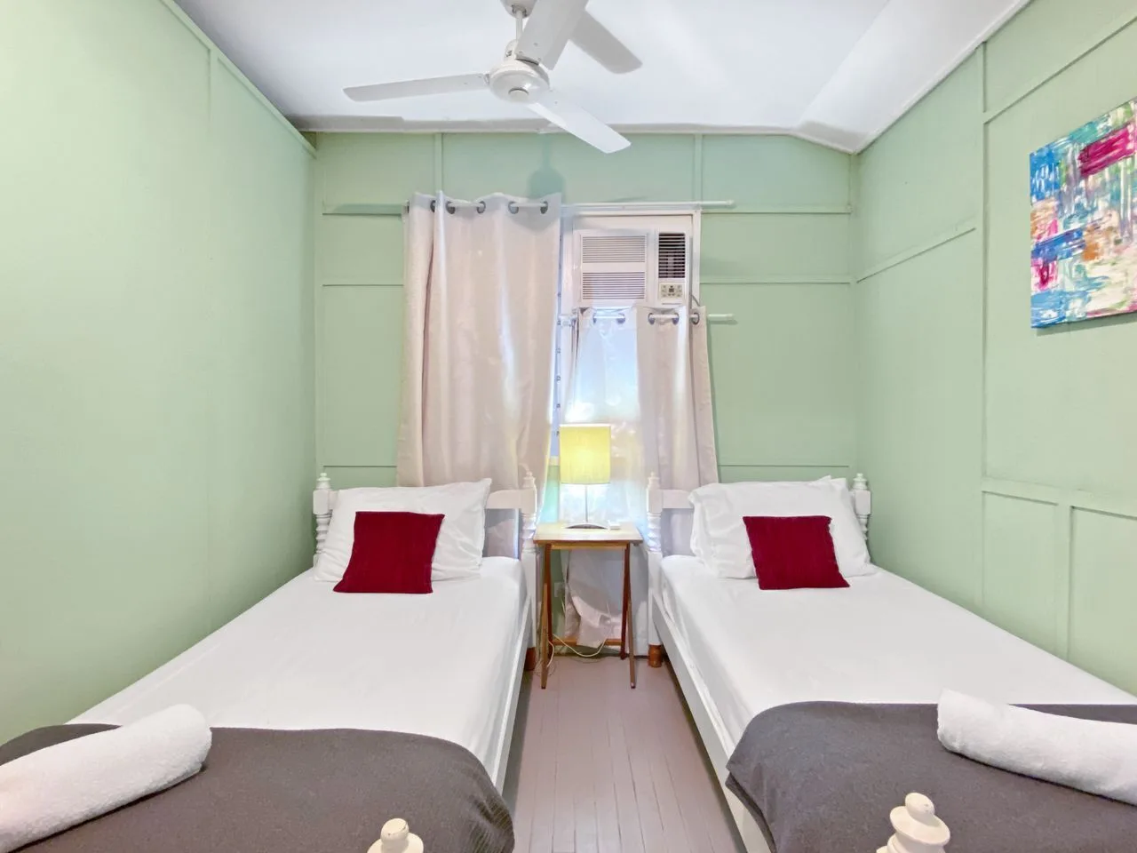 Dormitorio con dos camas individuales, una ventana y un ventilador de techo.