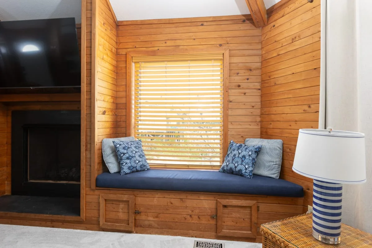 A wood-paneled room has a window with a cushioned seat beneath it.
