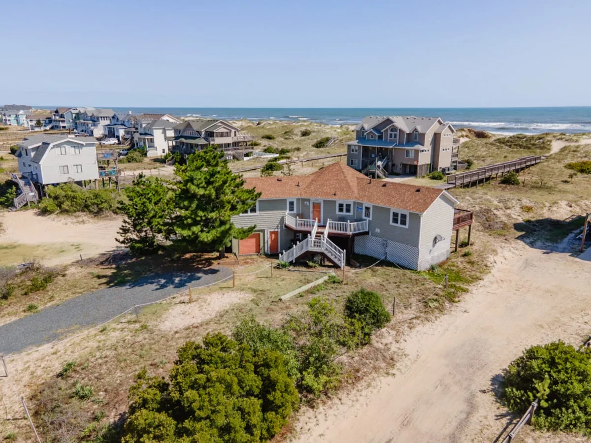 Coastal homes sit among sandy dunes, with the ocean visible in the background.