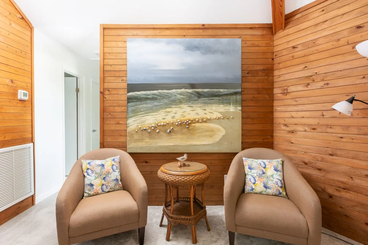 A sitting area with two cushioned seats and a large beach scene on the wall.