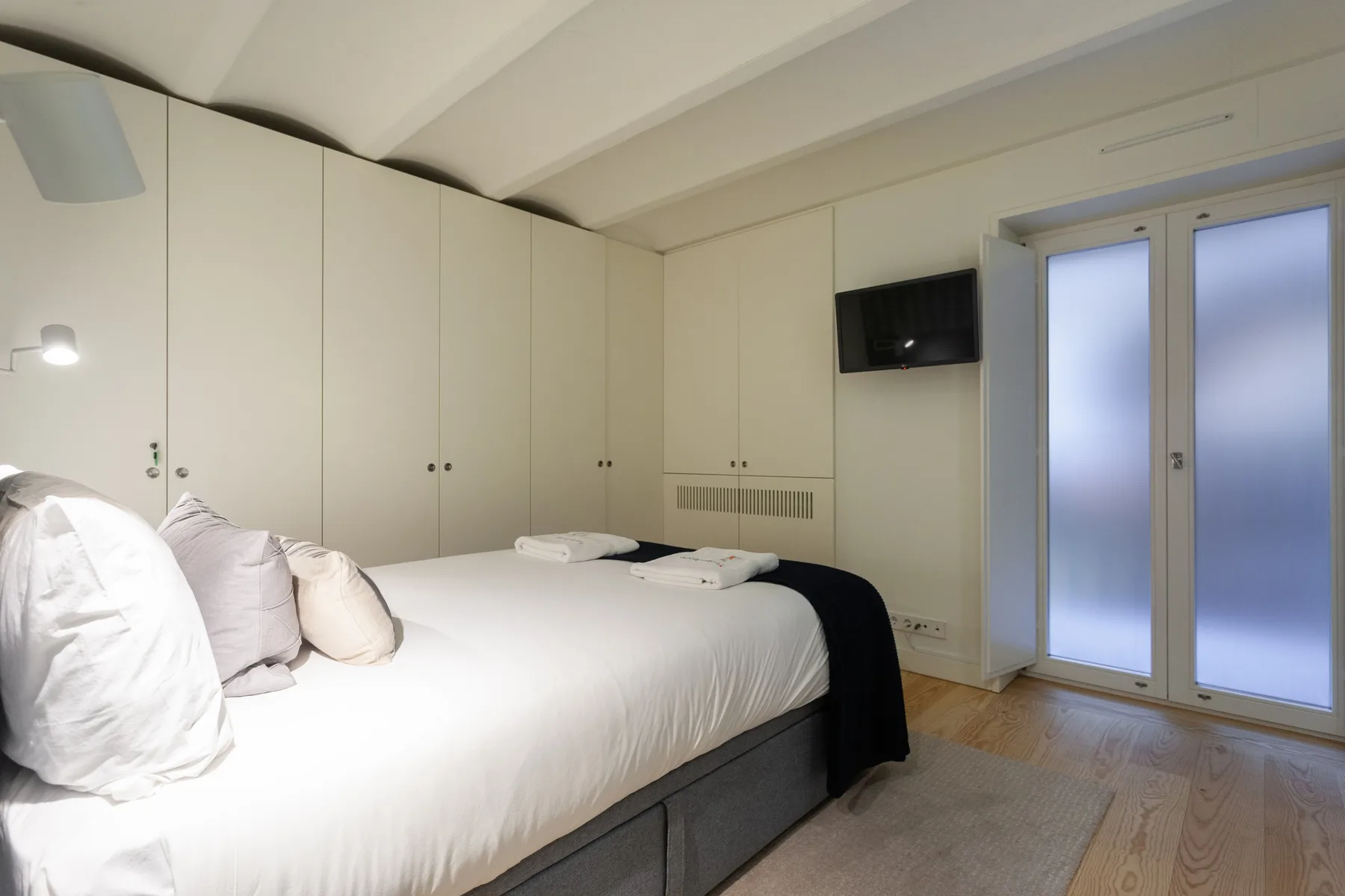 Un dormitorio con una cama bien hecha y puertas altas de vidrio esmerilado.