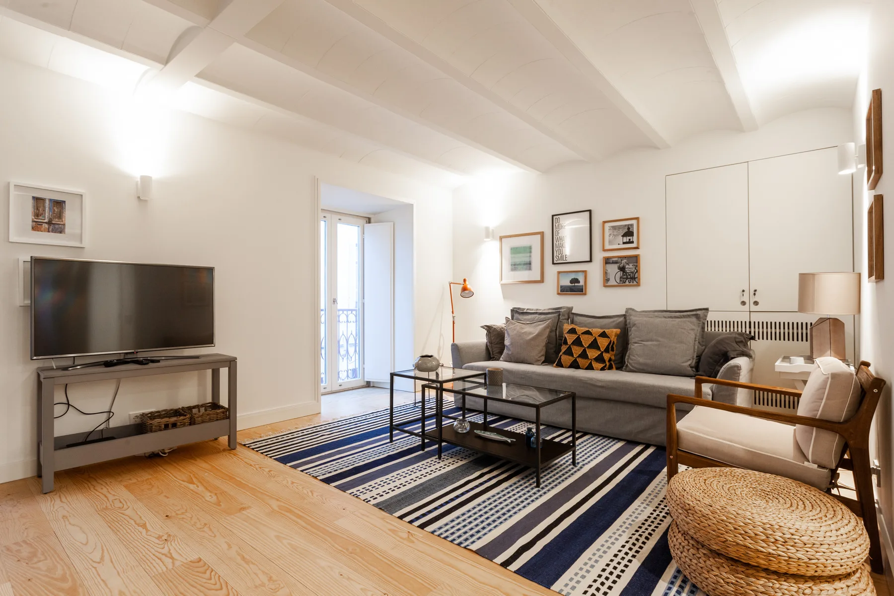Sala de estar con sofá gris, televisor y alfombra estampada.
