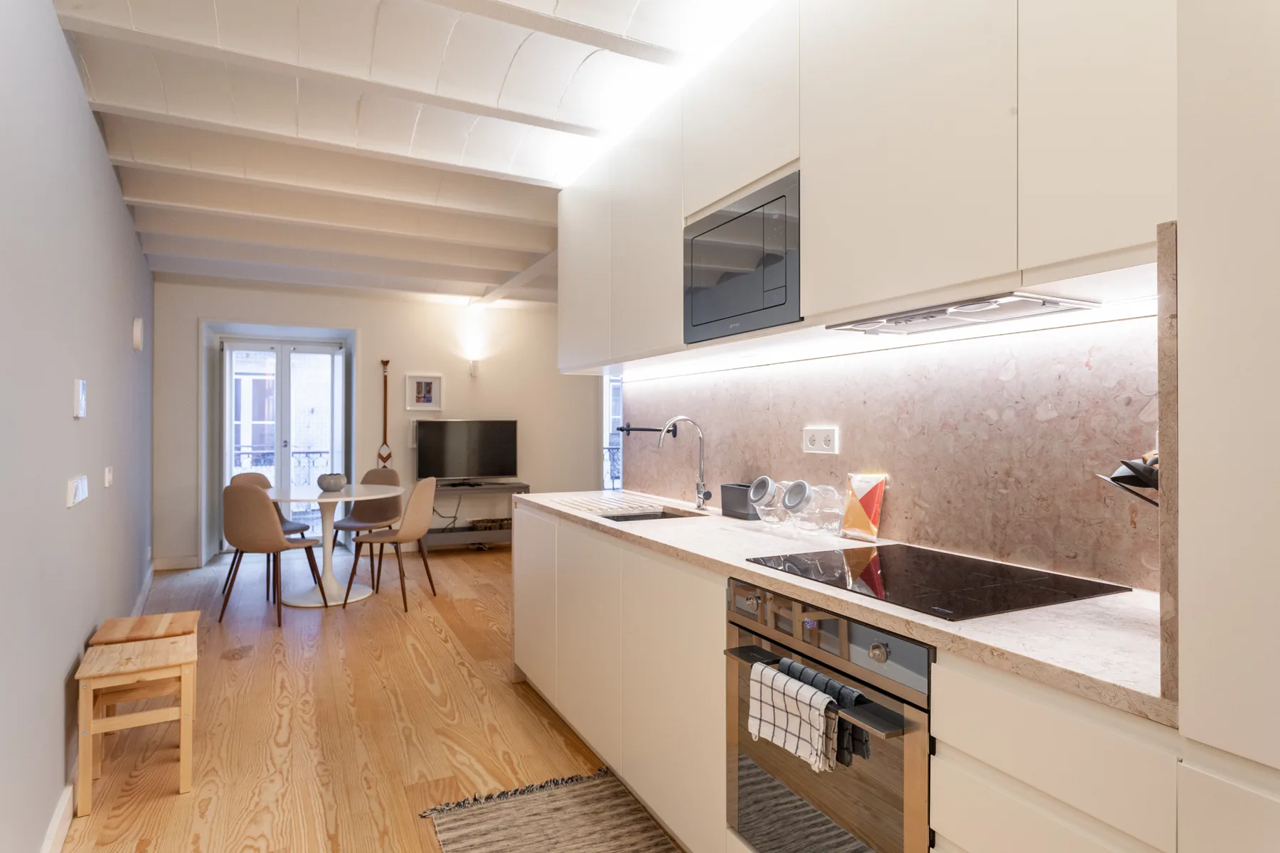 Una cocina abierta y luminosa con zona de comedor y un televisor al fondo.