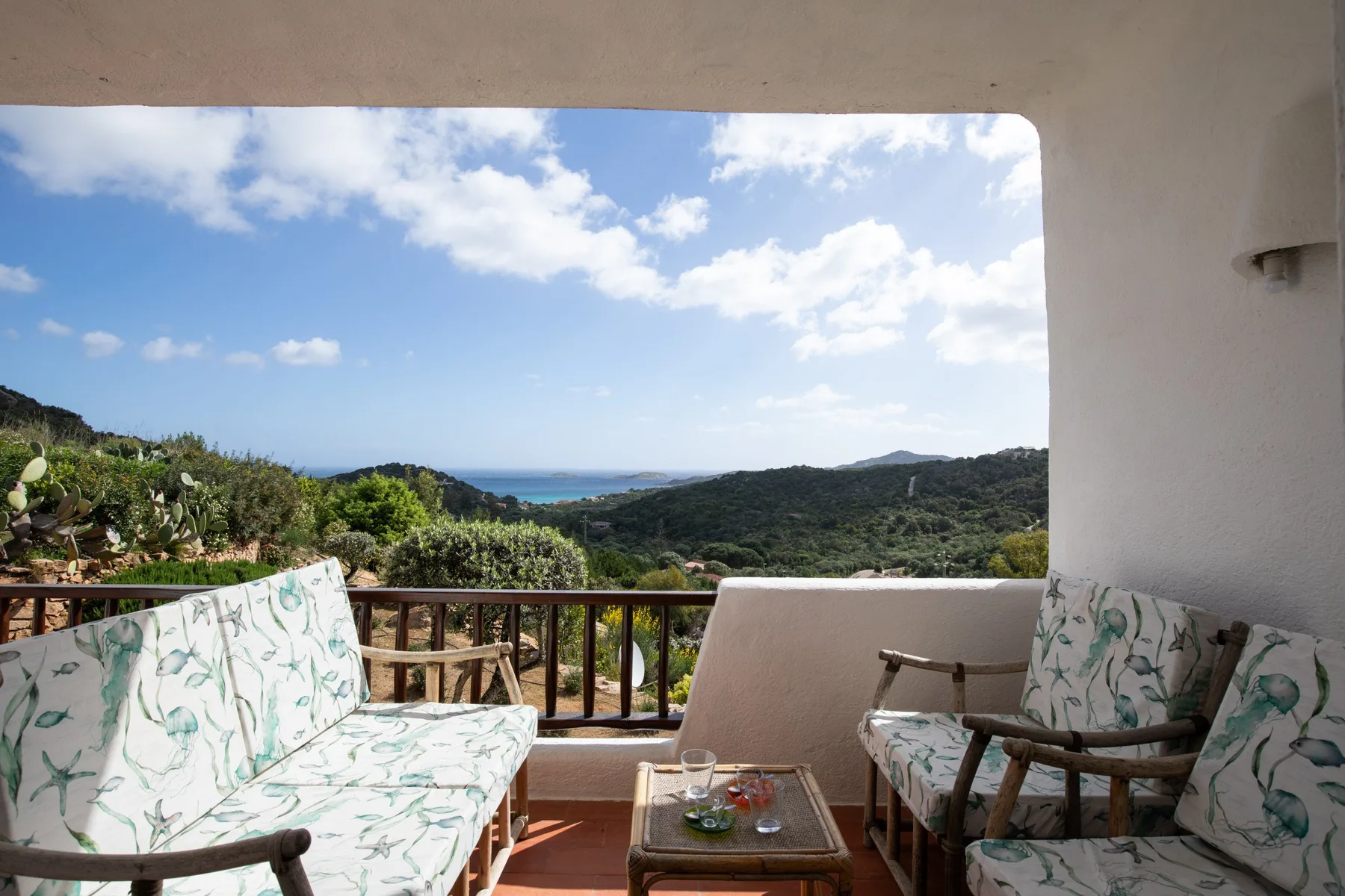 Covered terrace seating overlooks green hills and a glimpse of the sea.