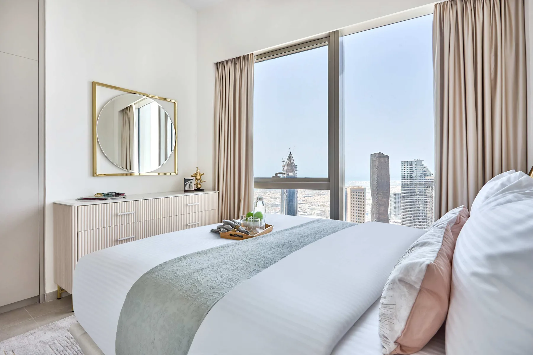 Un dormitorio luminoso con una cama tendida junto a una gran ventana con vistas a edificios de la ciudad.