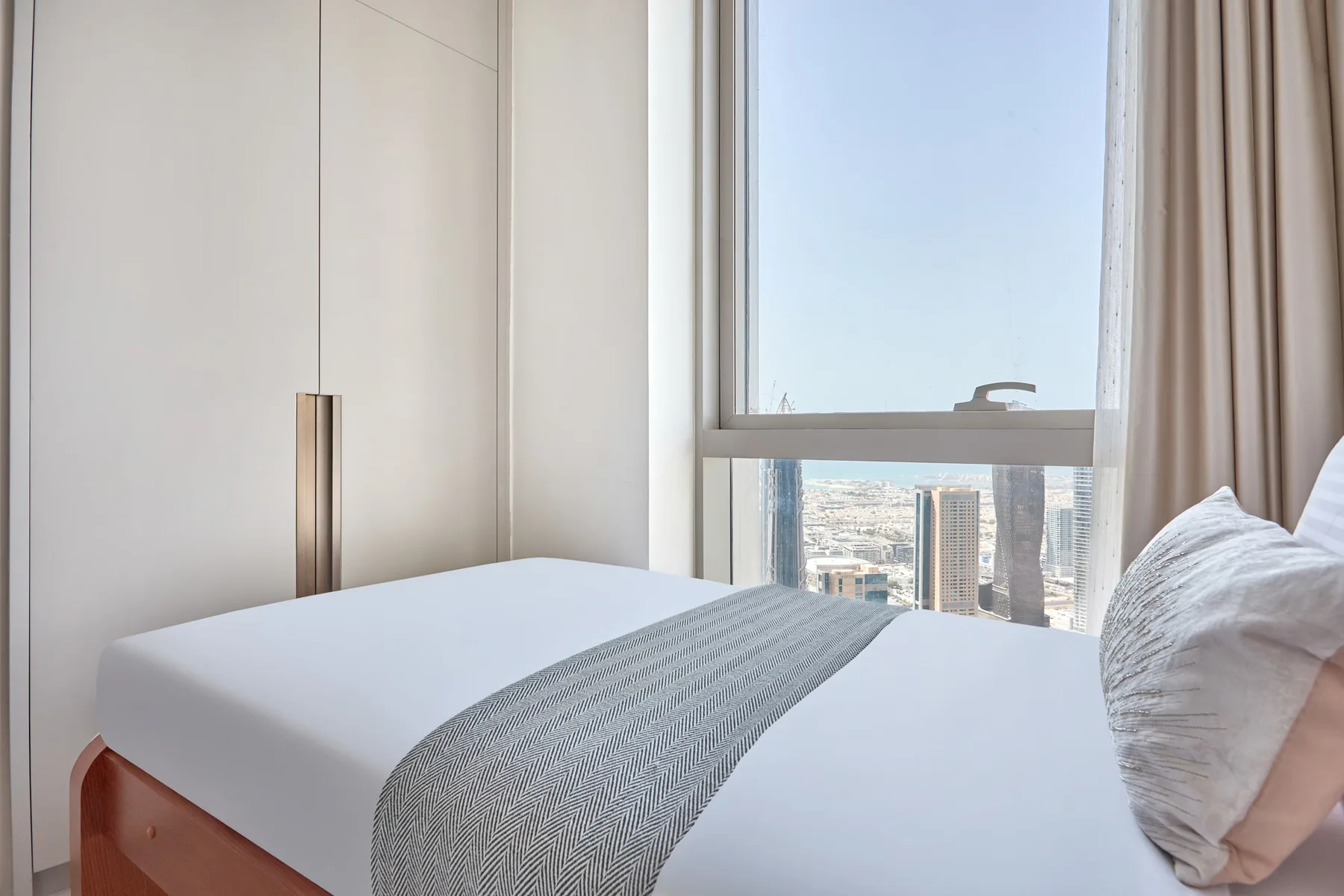 Un dormitorio luminoso con una cama arreglada junto a una ventana grande.