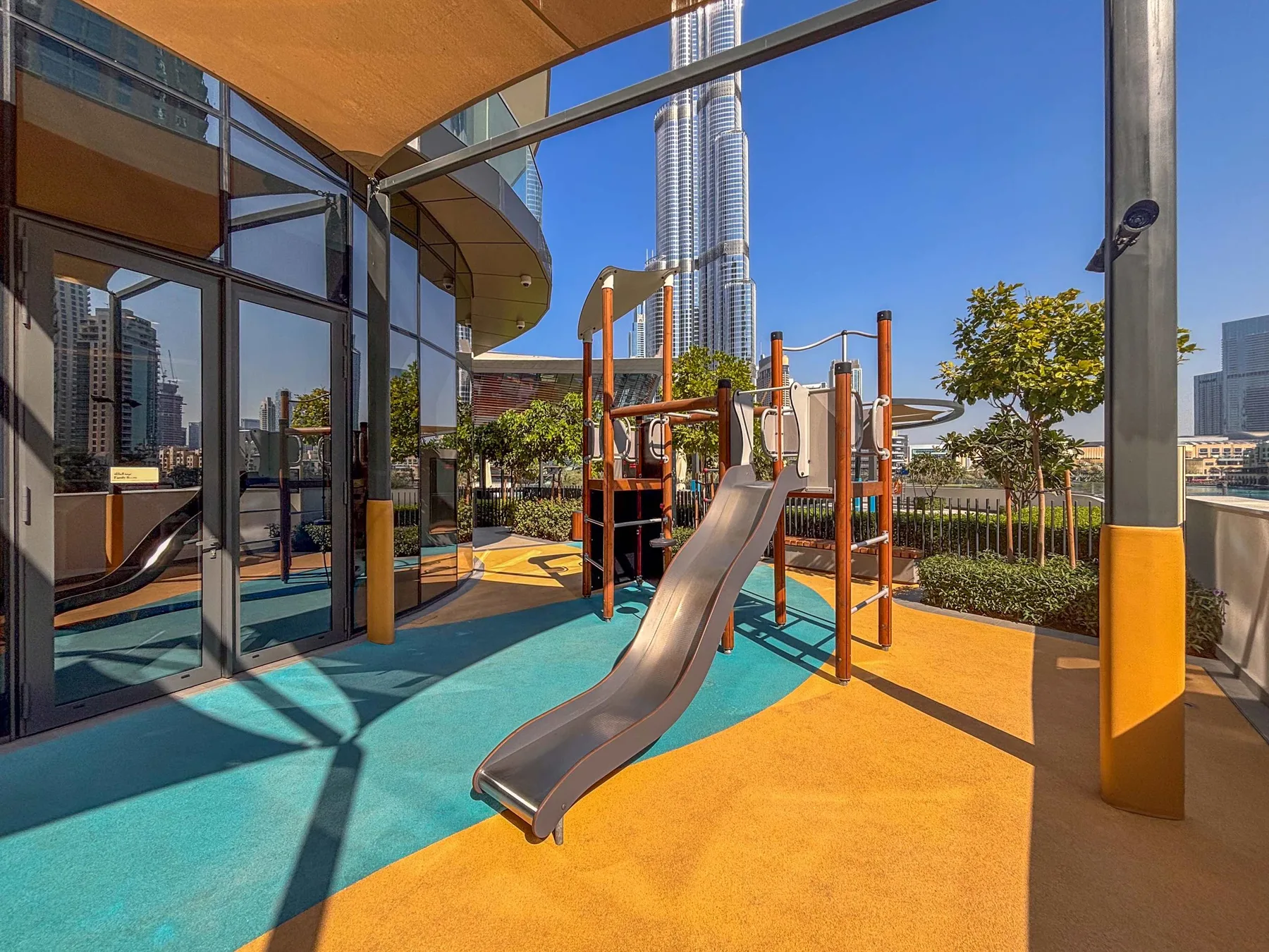 Un parque infantil al aire libre con un tobogán y equipo para trepar junto a un edificio de cristal.