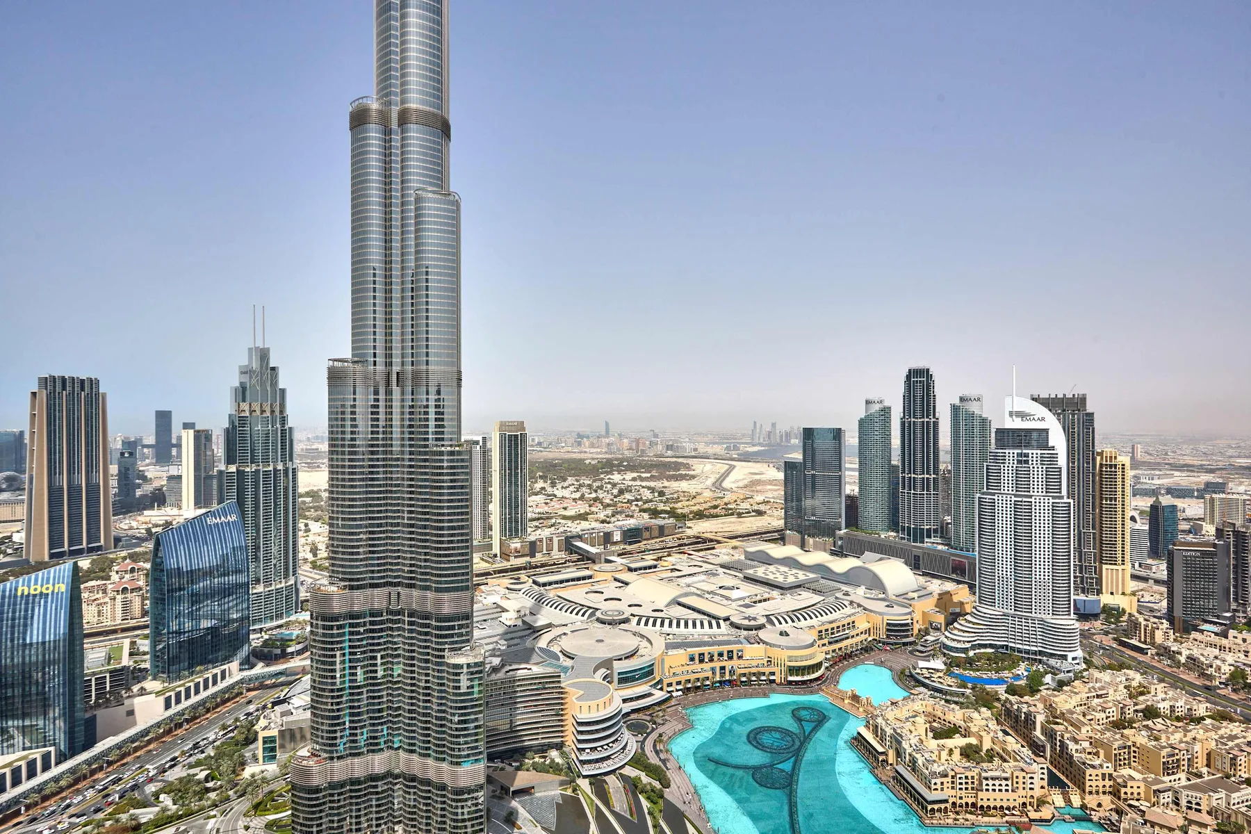 Un horizonte urbano con una torre muy alta en el centro y una piscina turquesa en primer plano.