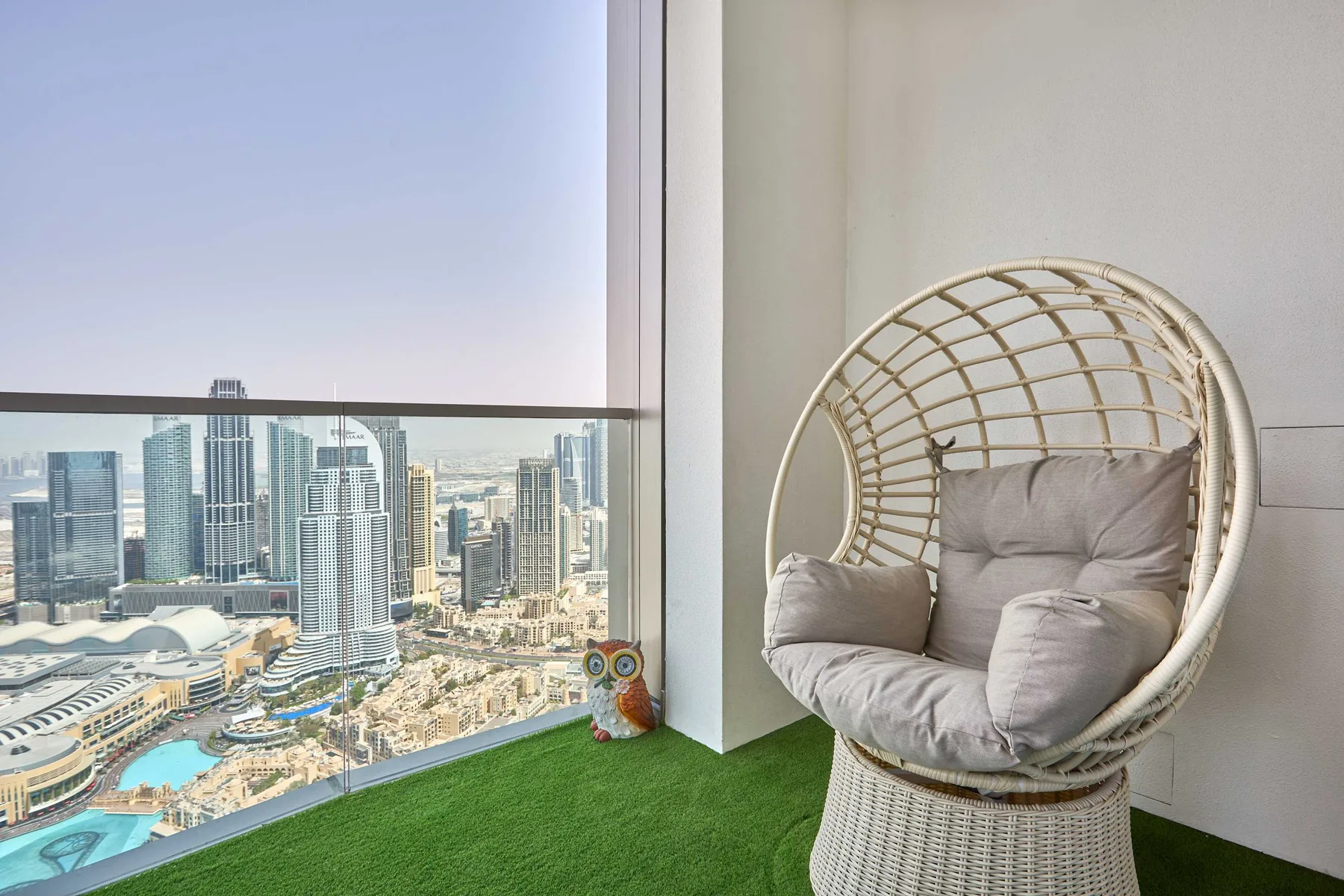 Una silla tejida con cojines está junto a una ventana amplia con vista a la ciudad.
