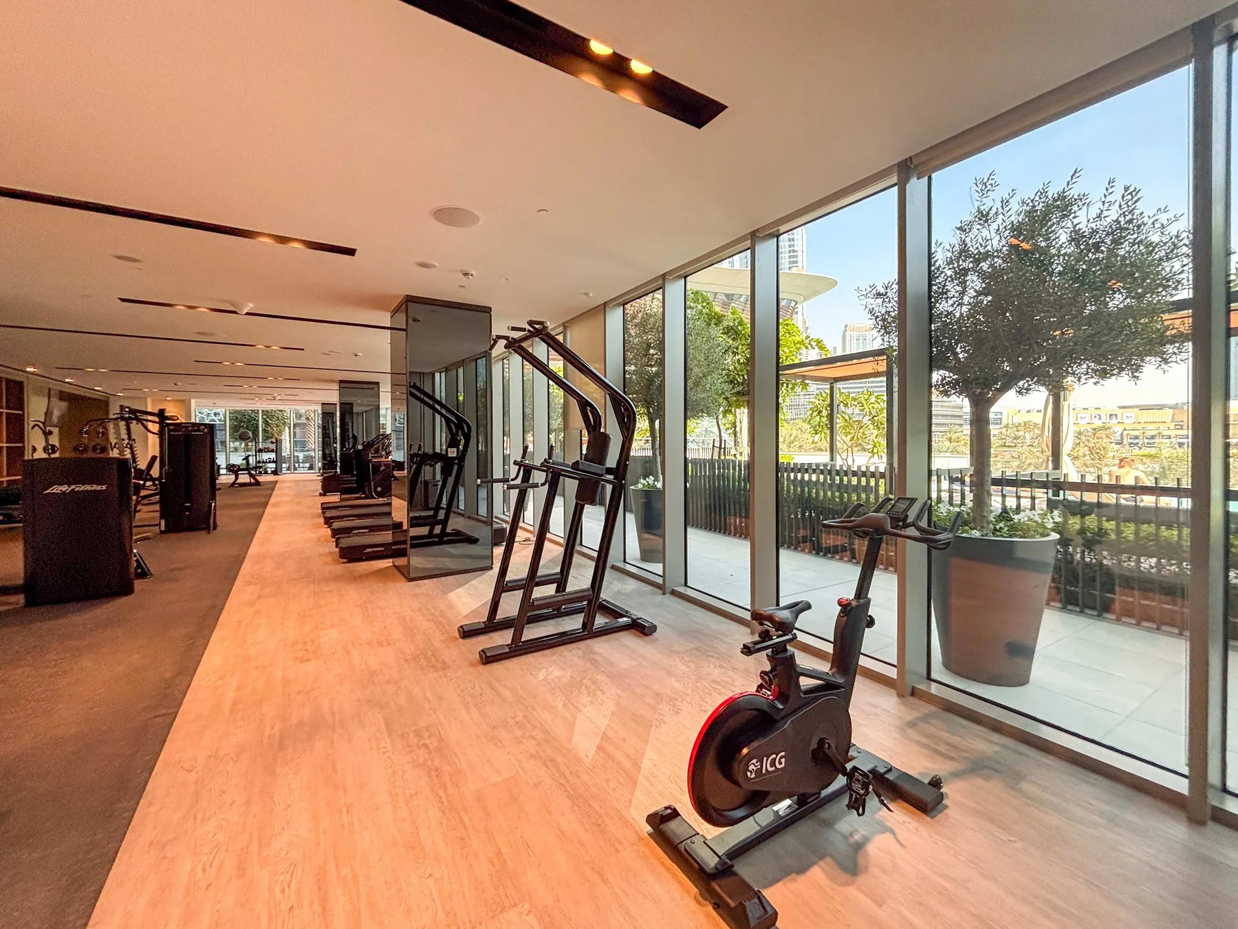 Un gimnasio luminoso con equipos de ejercicio junto a grandes ventanales.