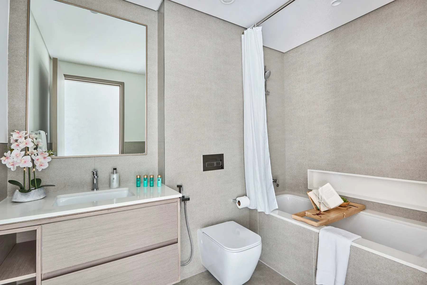 Un baño luminoso cuenta con lavabo, espejo de pared y bañera con cortina blanca.