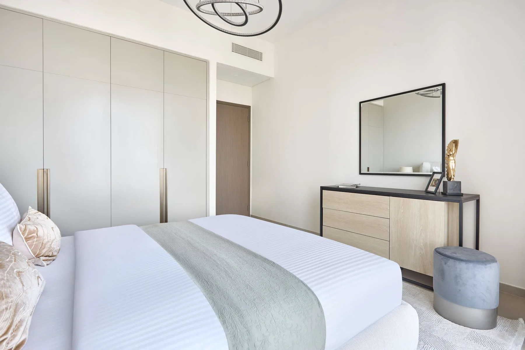 Un dormitorio luminoso con cama, armario y cómoda con espejo.