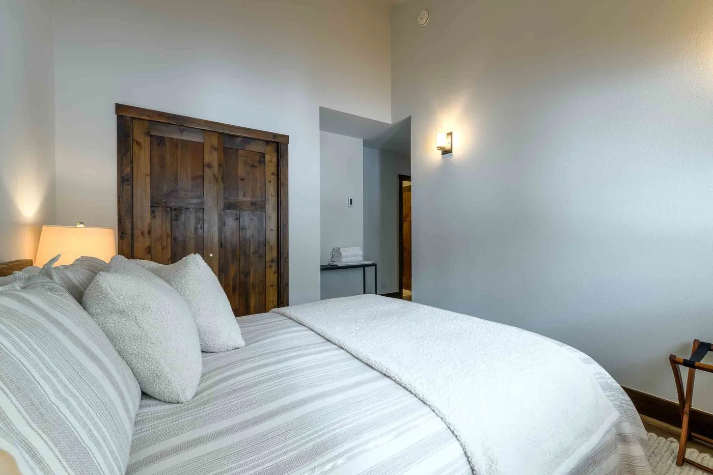 A bedroom with a neatly made bed and a dark wooden door.