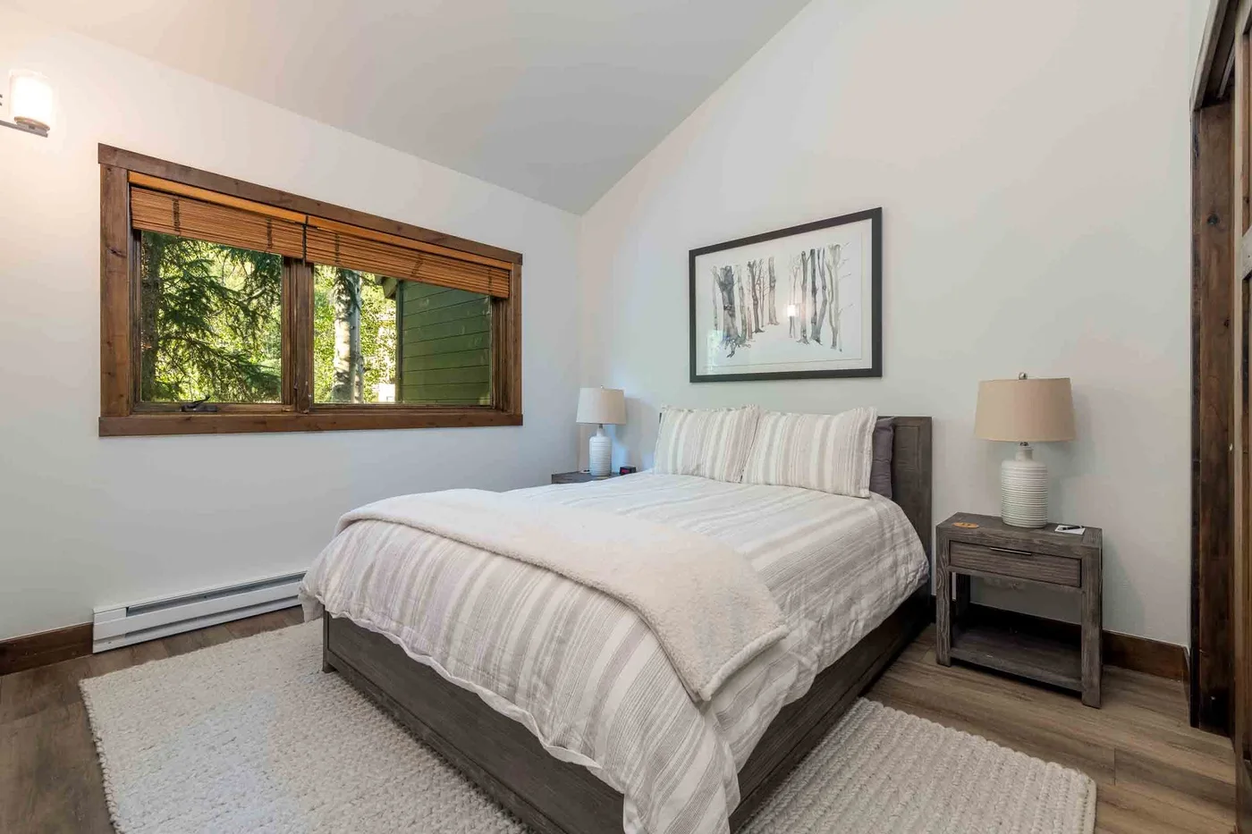 A bedroom with a neatly made bed, bedside tables, and a window overlooking trees.