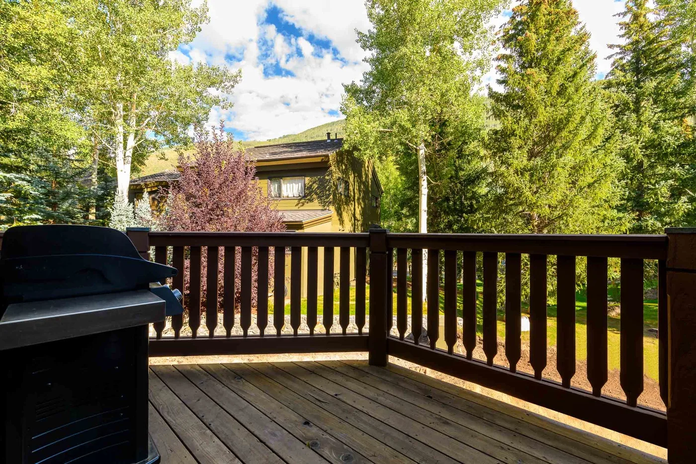 A wooden deck overlooks leafy trees, with an outdoor grill beside the railing.