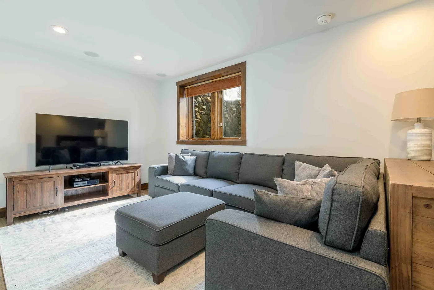 A living room with gray seating, a television, and a wooden media console.