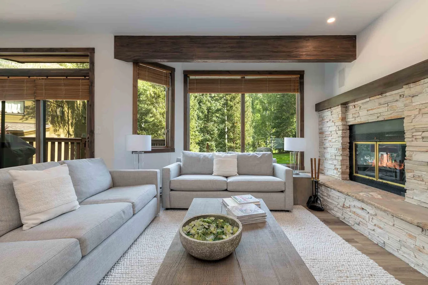 A living room with light seating, a coffee table, and a stone fireplace.