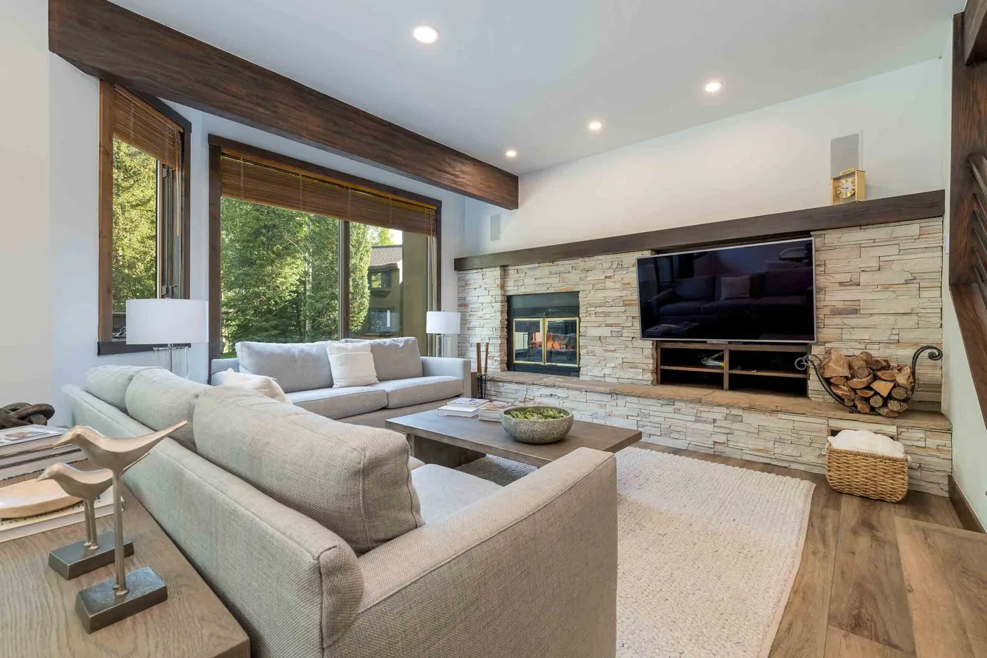 A living room with light seating facing a television and stone fireplace.