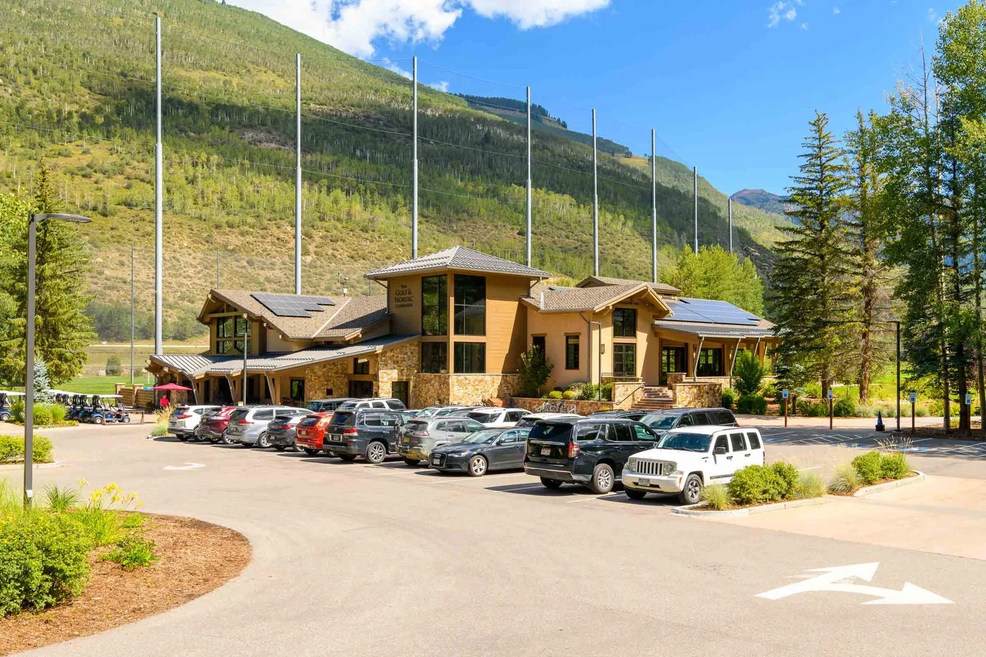 A lodge-style building stands beside a parking area, with wooded mountains behind it.