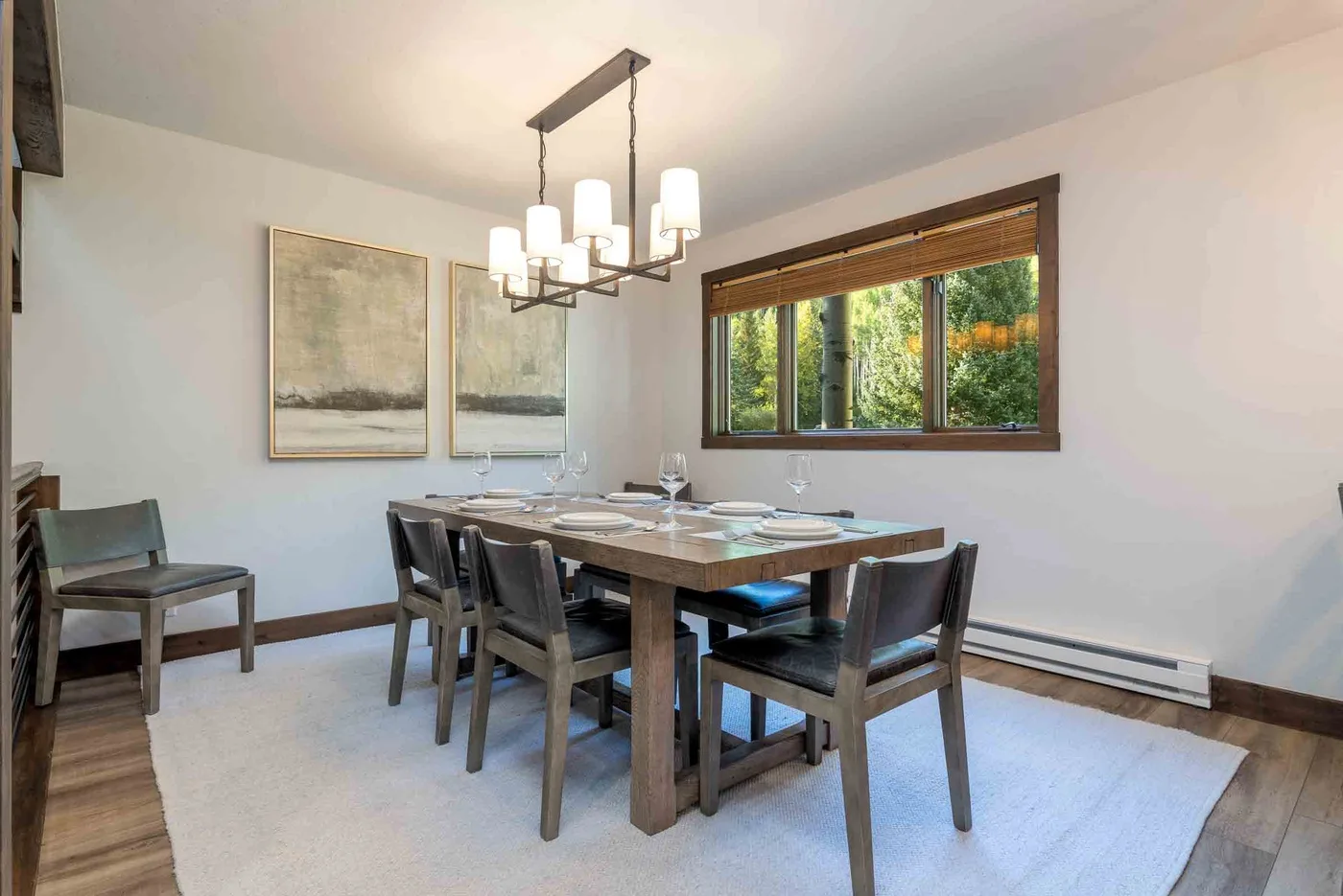 A dining room with a wooden table, chairs, and a hanging light fixture.