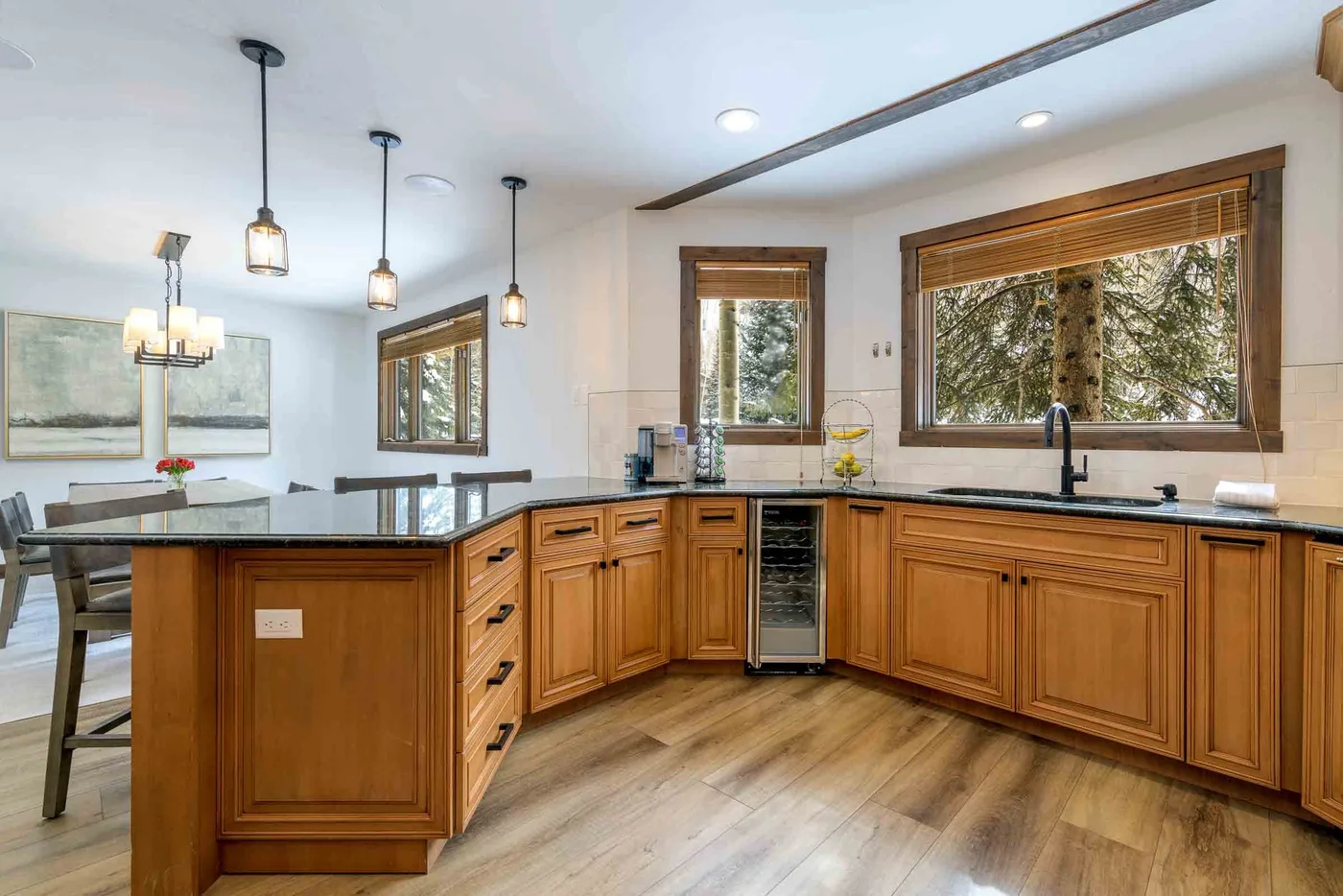 A bright kitchen with wooden cabinets, a large island, and windows overlooking trees.